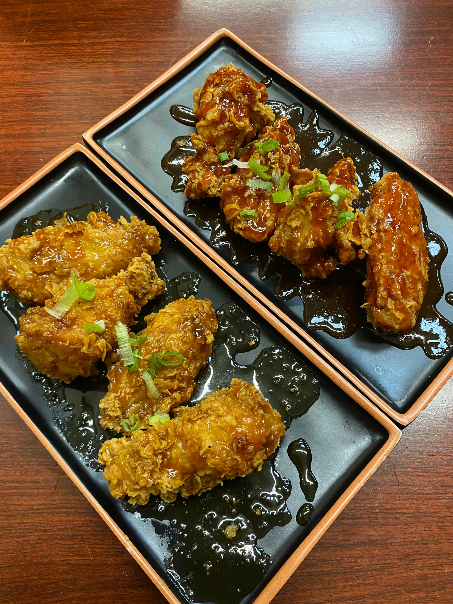 Two plates of Korean Fried Chicken, one with Mama's Spicy Korean Hot Sauce and one with Sweet Garlic Sauce.
